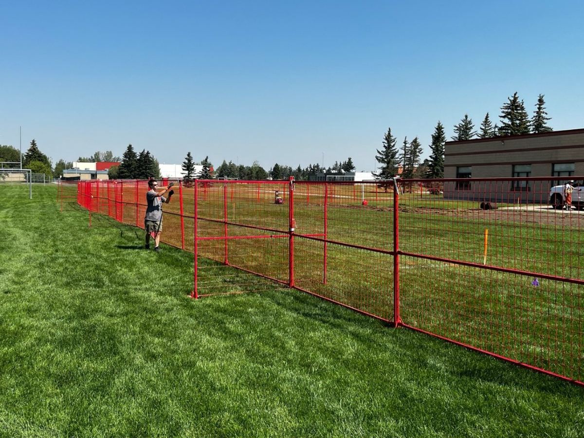 StructSure crew member installing red temporary fence panels on a Calgary job site