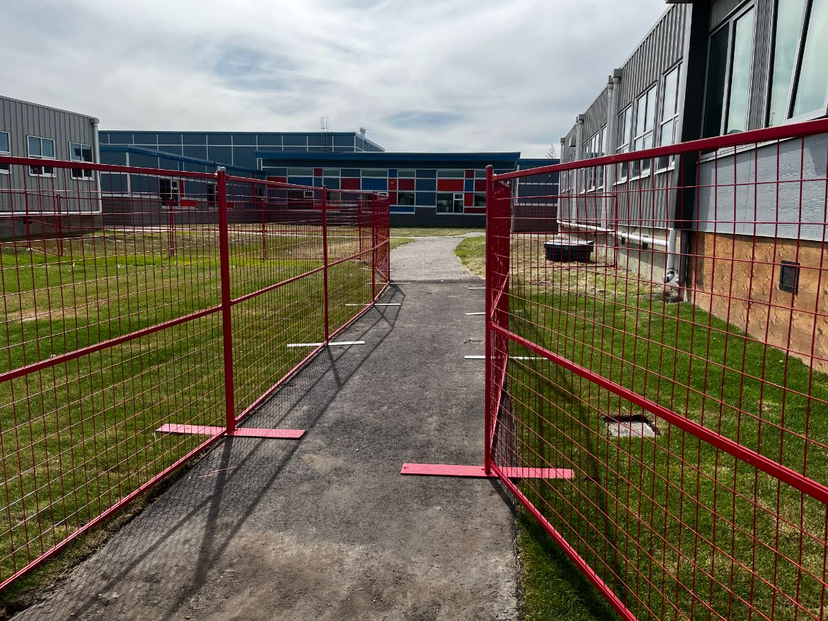 Yellow temporary fence panels around a school playground with blue slides