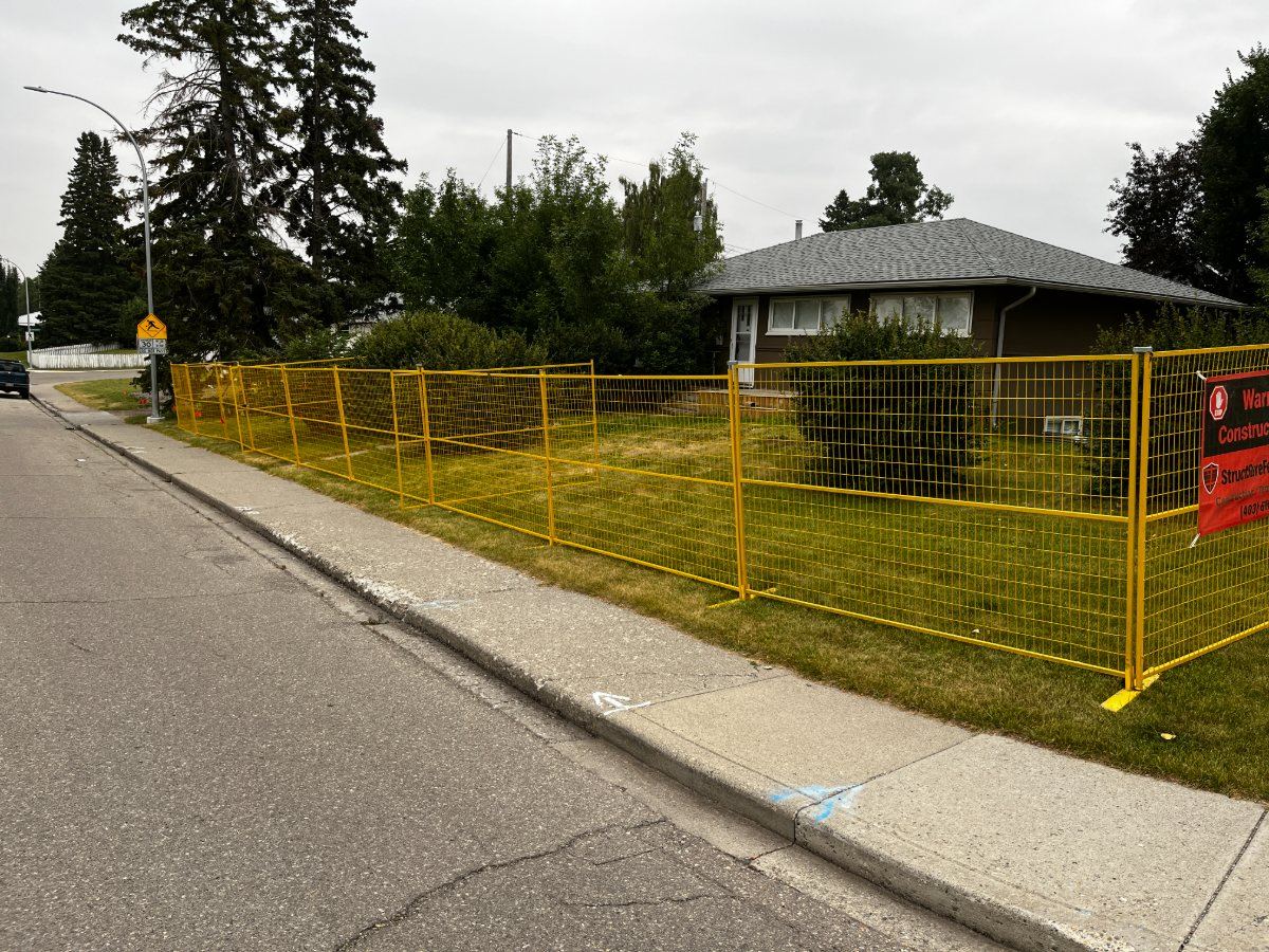 Yellow temporary fence securing a residential lot along a Calgary street