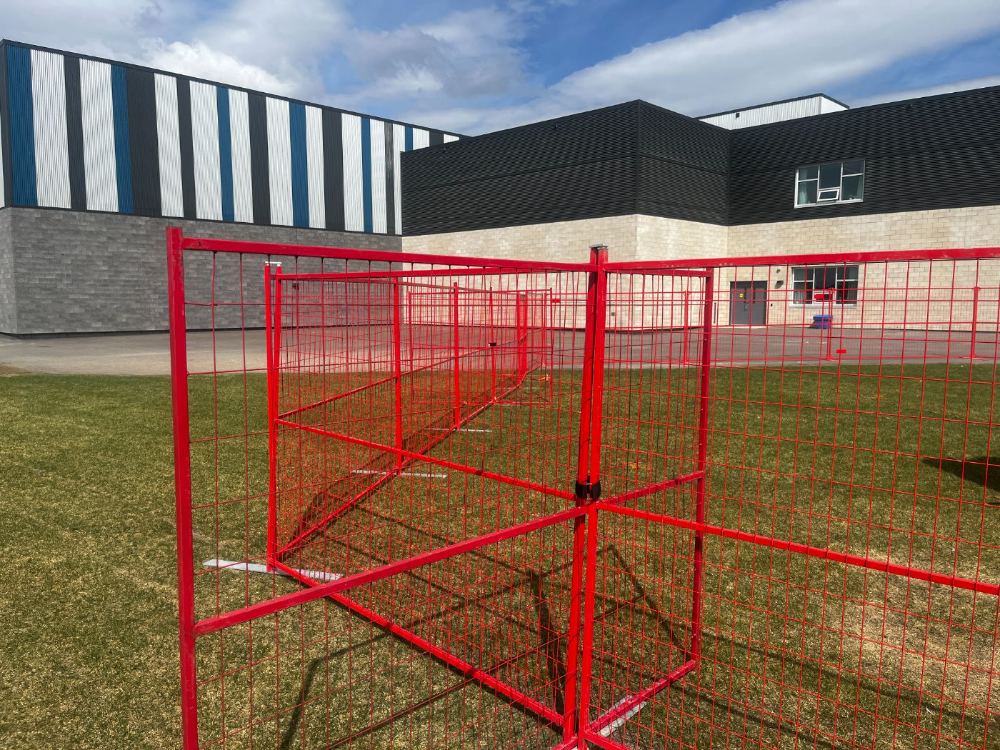 Red temporary fence panels cross-braced at a corner to hold the run stable on grass