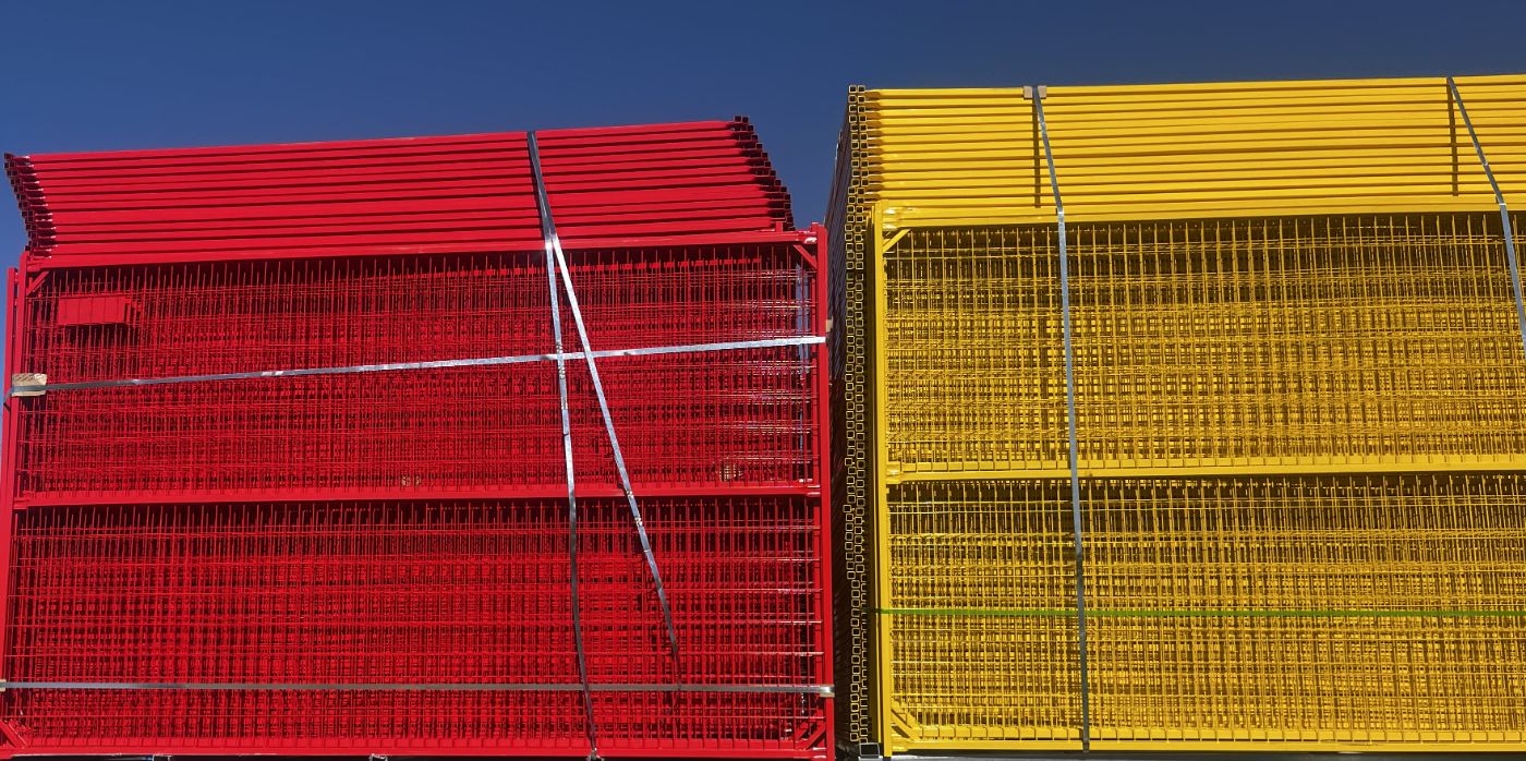 Bundled red and yellow temporary fence panels stacked against a blue sky