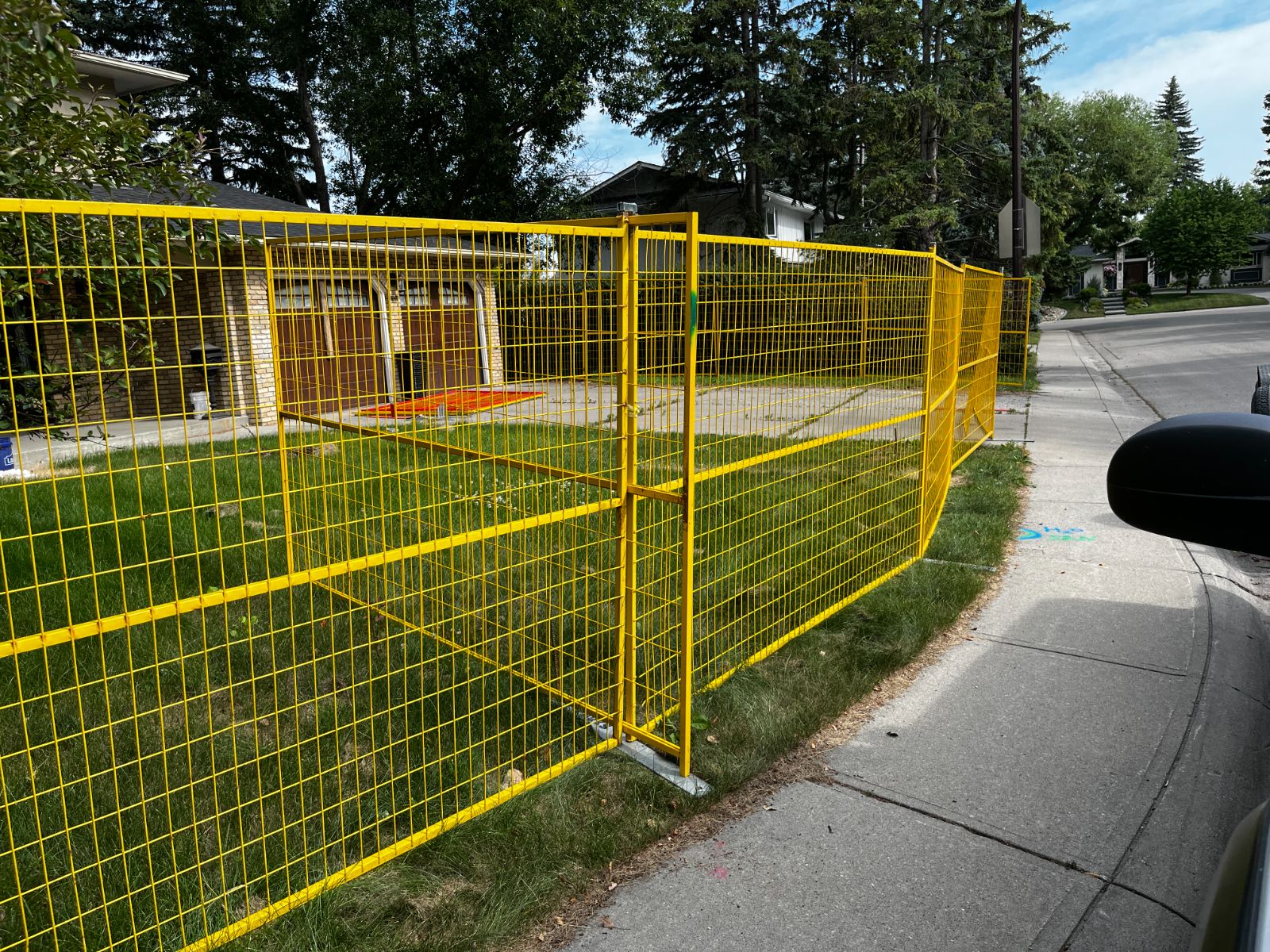 Yellow temporary fence panels along a residential sidewalk corner
